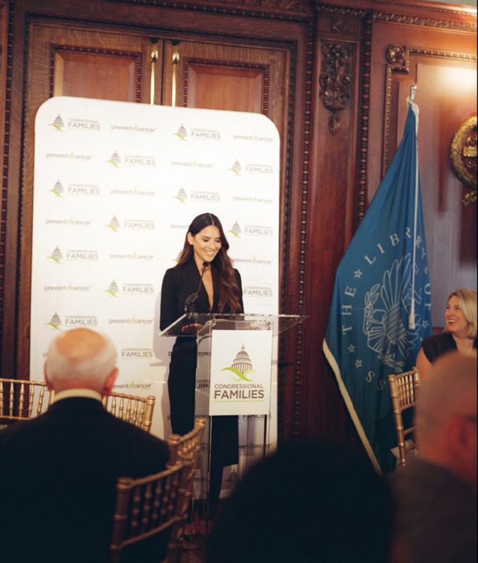 Actress Olivia Munn stands at the podium with her award at the 2025 Congressional Families Luncheon Award ceremony.