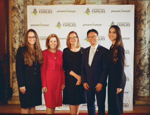Five people stand in front of a backdrop to take a photo together, smiling.