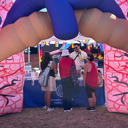 A information table is set up outdoors with a giant inflatable lung set up around it. A white man is standing behind the table talking to three people who are facing away from the camera.