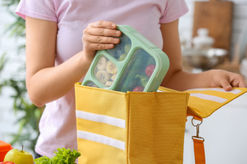 A mother places a packed lunchbox into her child's bag for school.