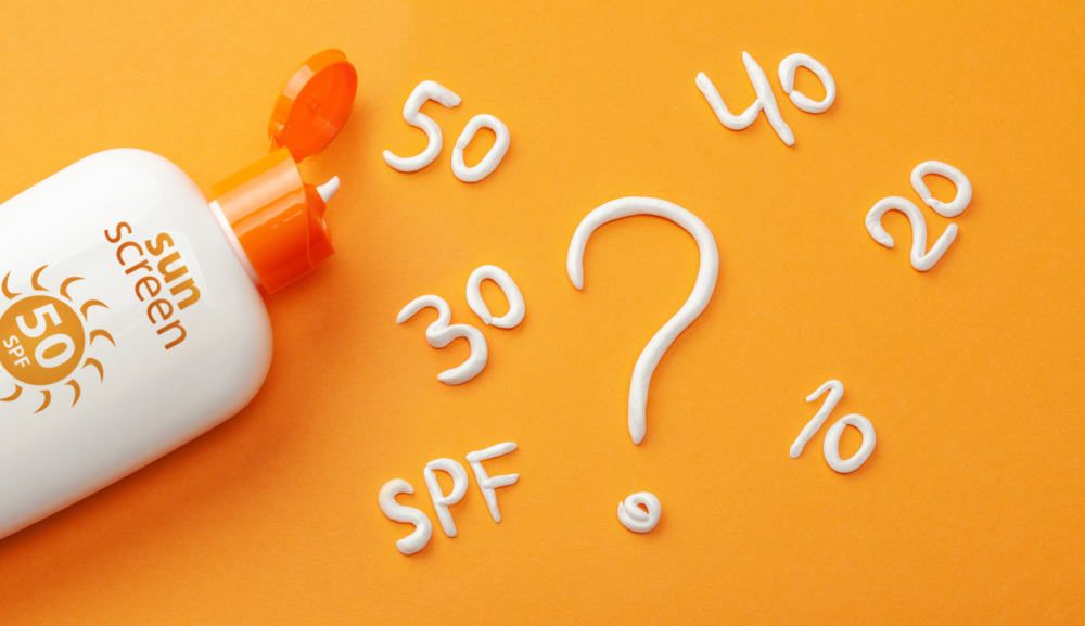 Sunscreen on orange background. Plastic bottle of sun protection and white cream in the form of question mark and numbers SPF. How to choose a sunscreen.