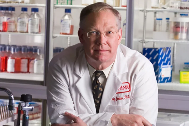 Dr. Craig Jordan, wearing a lab coat and posing in his research lab