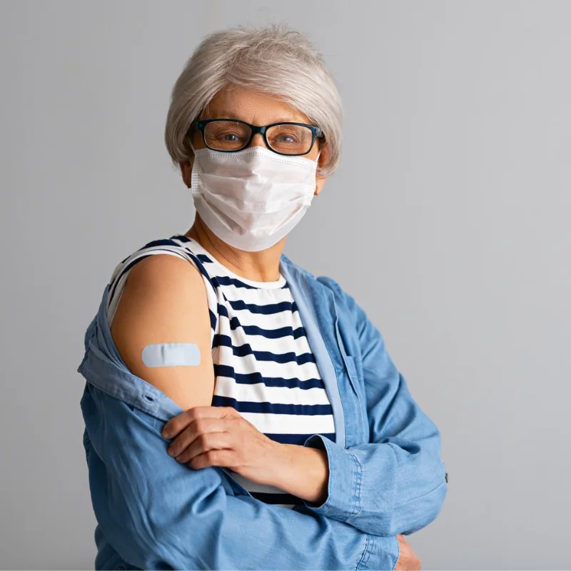 Woman wearing PPE mask has a bandaid on her arm from receiving a shot.